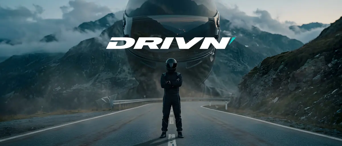 DRIVN key visual: a driver in a race suit stands on a mountain road, a giant helmet and the DRIVN logo behind him